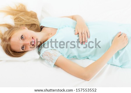 Happy long-haired pregnancy woman in nightdress lying on bed in bedroom