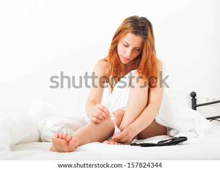 Beautiful red-haired girl cares for toenails with nail lacquer