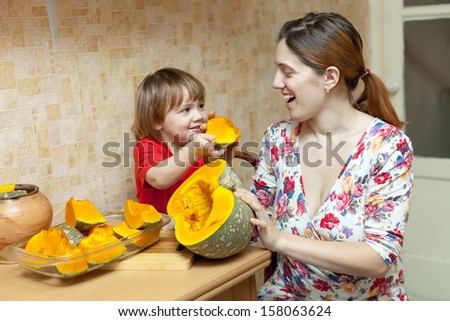Happy mother with child cooks pumpkin  in kitchen at home. Focus on woman