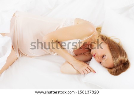 Long-haired pregnant woman sleeping on white pillow in bed at home