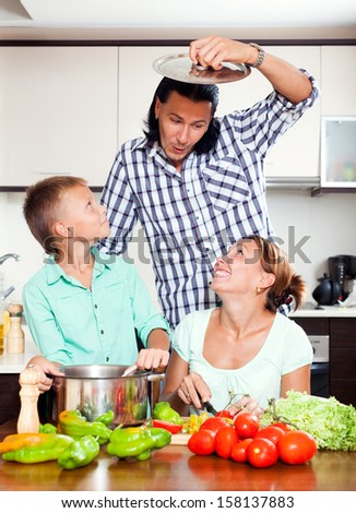 Funny parents with teenager son cooking vegetarian lunch in home kitchen