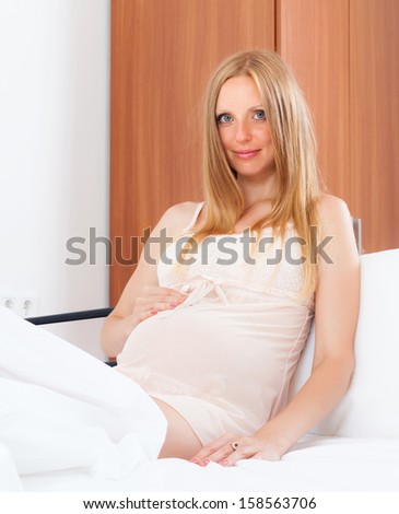 Sitting long-haired pregnancy woman in nightdress on bed