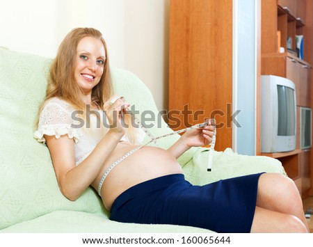 Pregnant young woman measuring waist with tape measure at home