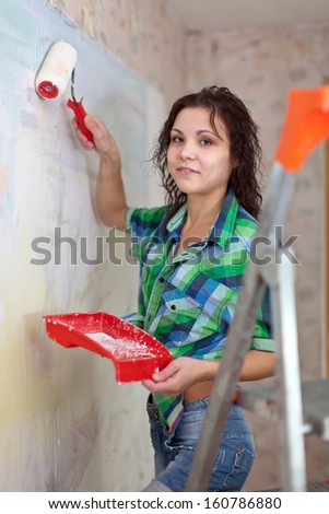 Happy girl paints wall with roller at home