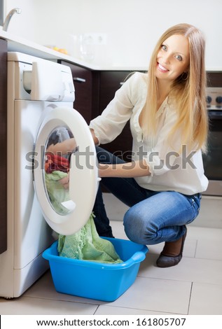 Home laundry. Happy blonde woman loading clothes into the washing machine