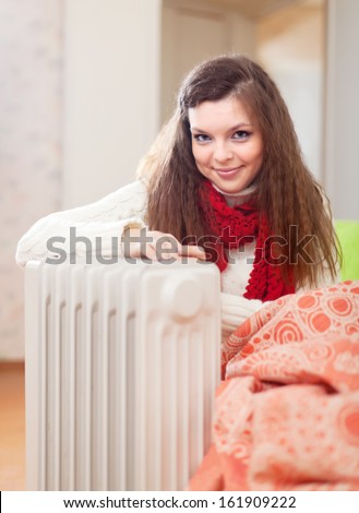 Smiling long-haired woman near oil heater at her home