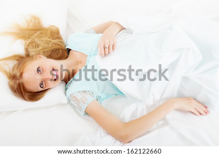 Cheerful long-haired girl in nightshirt lying on white sheet
