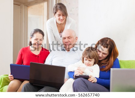 Happy multigeneration family uses few portable computers in home interior