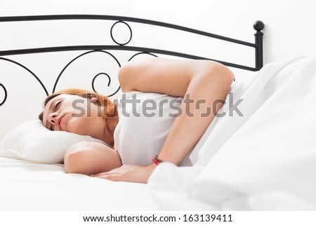 Ginger long-haired girl sleeping on white pillow in bed at home
