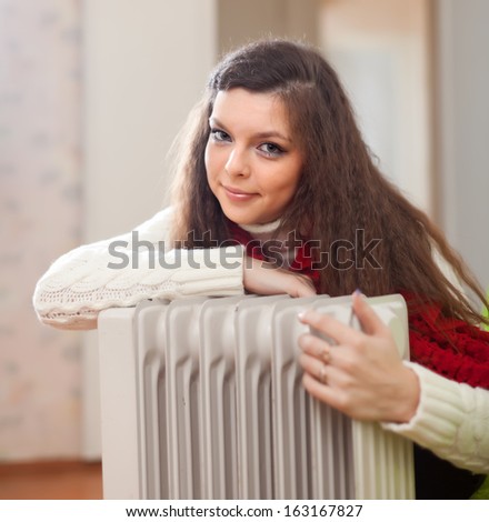Portrait of long-haired woman near oil heater at her home