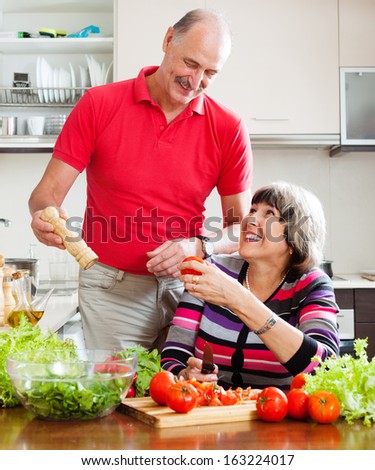 Happy elderly couple cooking with tomatoes in home kitchen