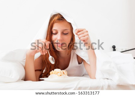 woman eating sweet cake under sheet in bed