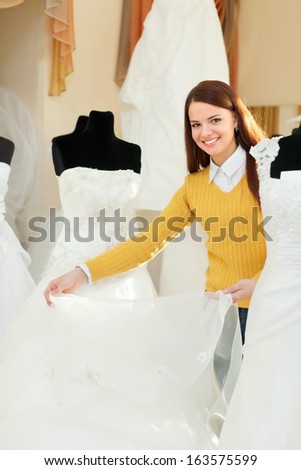 Smiling pretty bride chooses bridal gown in wedding boutique