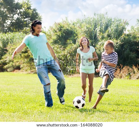 Middle-aged couple and teenager son playing with soccer ball  at summer park