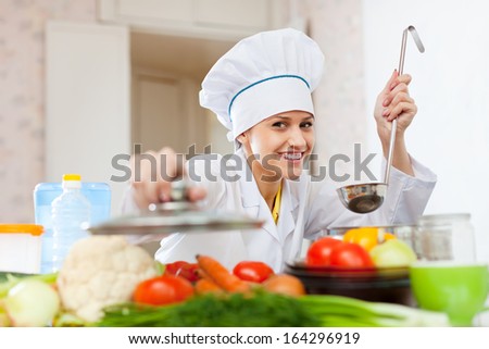 Happy female cook  in white toque works at kitchen