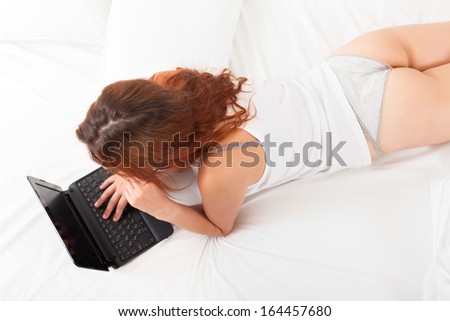 Top view of red-haired woman with laptop on white sheet in bed at home