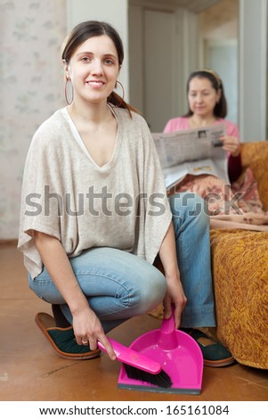 Clean up  adult daughter, while her mature mother reads newspaper on the sofa at home