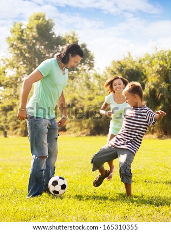 Happy parents with teenage son playing with soccer ball at summer park