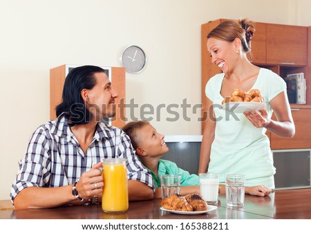Smiling woman serves croissants  her husband and son in morning breakfast