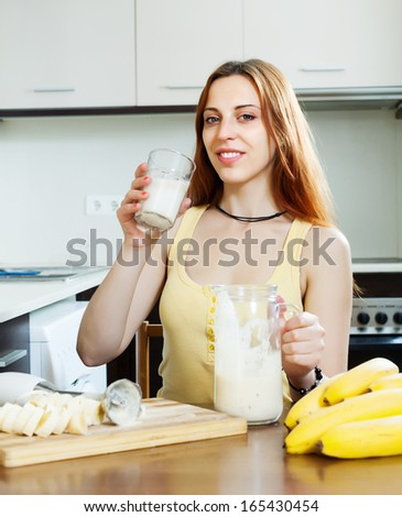 girl in yellow drinking milk shake with bananas at home kitchen