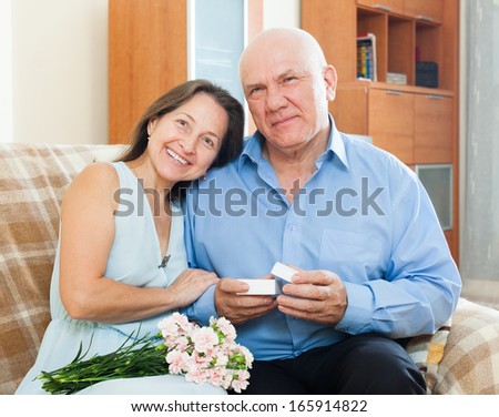 Mature man presenting smiling woman jewel in box  at home