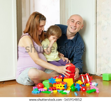 Happy parents and child plays with plastic toys in home