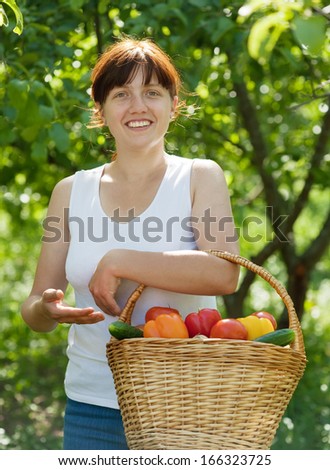 Happy young woman with basket of harvested vegetables in garden