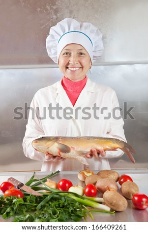 Cook woman with carp fish in kitchen