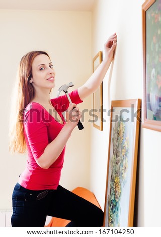 woman hanging the art pictures on wall at home