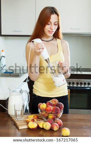 long-haired woman cooking beverages with electric blender from peaches at  kitchen