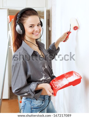 Happy young woman in headphones  makes repairs in the apartment