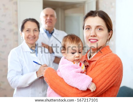 Portrait of happy mother with baby in arms against doctors in background