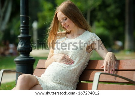 Happy pregnancy woman sitting on bench in summer park