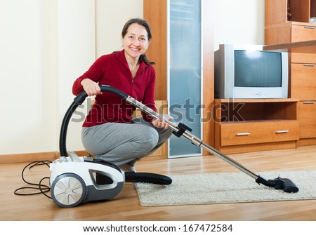 Happy mature woman with vacuum cleaner  in living room