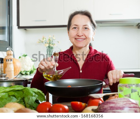 Happy mature woman pouring oil into  skillet at kitchen