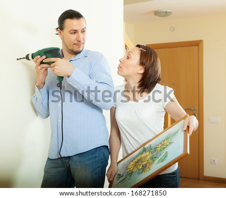 Man and woman  hanging   picture on wall at home