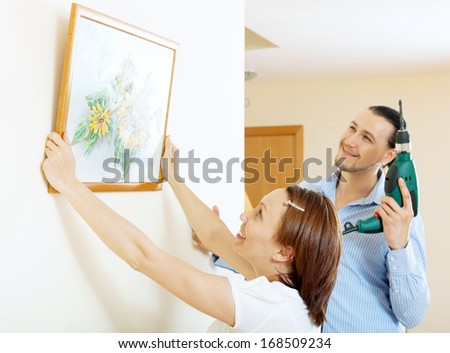 middle-aged man and woman  hanging  art picture in frame on wall at home