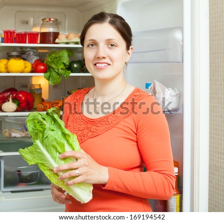 Young woman with fresh  lettuce near refrigerator  at home