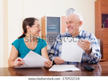 Happy mature couple holding financial documents at home