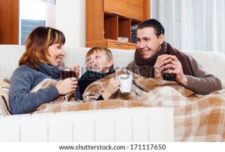 Happy parents and teenage son with cups of tea warming near warm calorifer in home