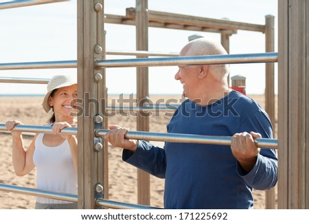 senior guy and mature girl training with pull-up bar at playground
