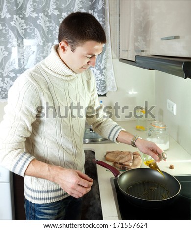Handsome man cooking raw steak of porbeagle in frying pan at home kitchen