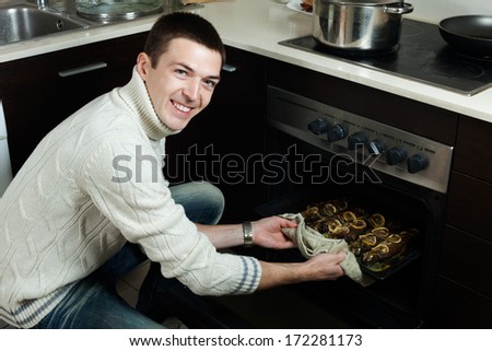Happy handsome man takes the cooked fish on a baking sheet from the oven