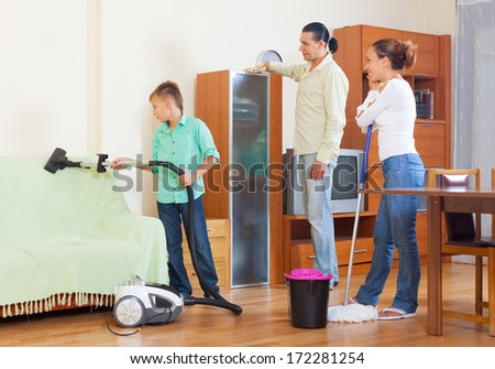 Couple and teenager boy cleaning with vacuum cleaner in living room