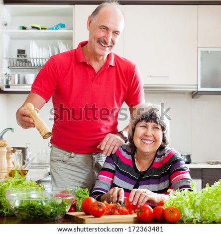 happy senior man in red and  woman cooking lunch together in  kitchen