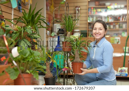 Happy mature woman with Nolina plant surrounded by different flowers in flower store