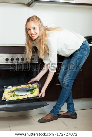 Smiling woman cooking fish in oven at home