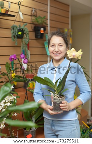 Happy mature woman with orchid in flower store