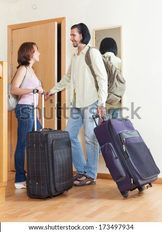 Couple with luggage looking in mirror near door in home