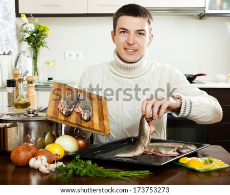 Smiling guy cooking  fish  in frying pan at  kitchen